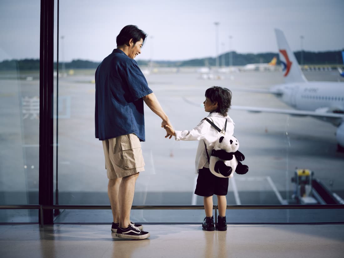 Pai e filho de mãos dadas olhando os aviões pela janela do aeroporto